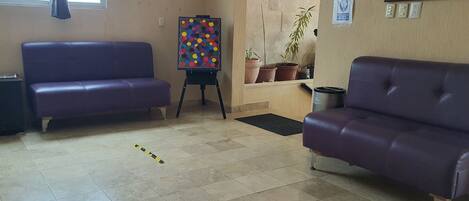 A room with two purple sofas, a colorful abstract painting on an easel, and several potted plants.