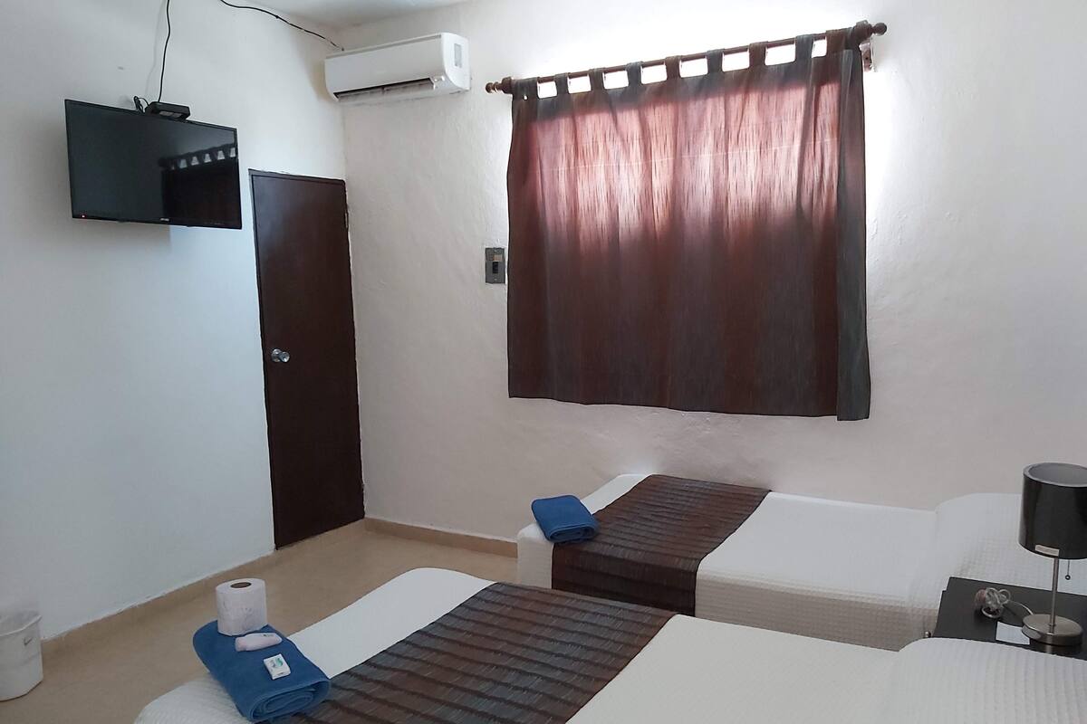 Una habitación de hotel con dos camas, televisión, aire acondicionado y una cortina.