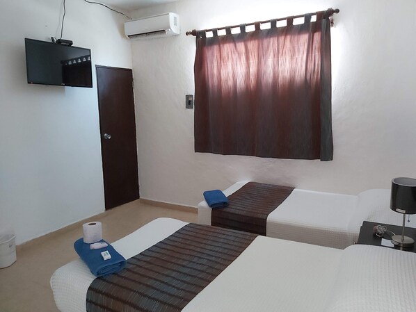 A hotel room with two beds, a TV, an air conditioner, and a curtain. - Hotel Villa Fontana (Chetumal)