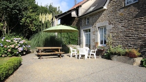 A stone building with a gravel patio, a wooden bench, a table with chairs, and an umbrella.