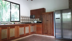 A kitchen with wooden cabinets, a microwave, a toaster, and a stainless steel refrigerator. - OceanBlue Samara Lodge (Sámara)