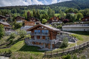 A chalet-style building with a stone foundation, wooden balconies, and a stone retaining wall. - Chalet Oak Tree amazing, sauna, ski-in/out (Haute-Nendaz)