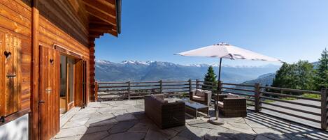 A wooden cabin with a stone patio, outdoor furniture, and a view of snow-capped mountains.