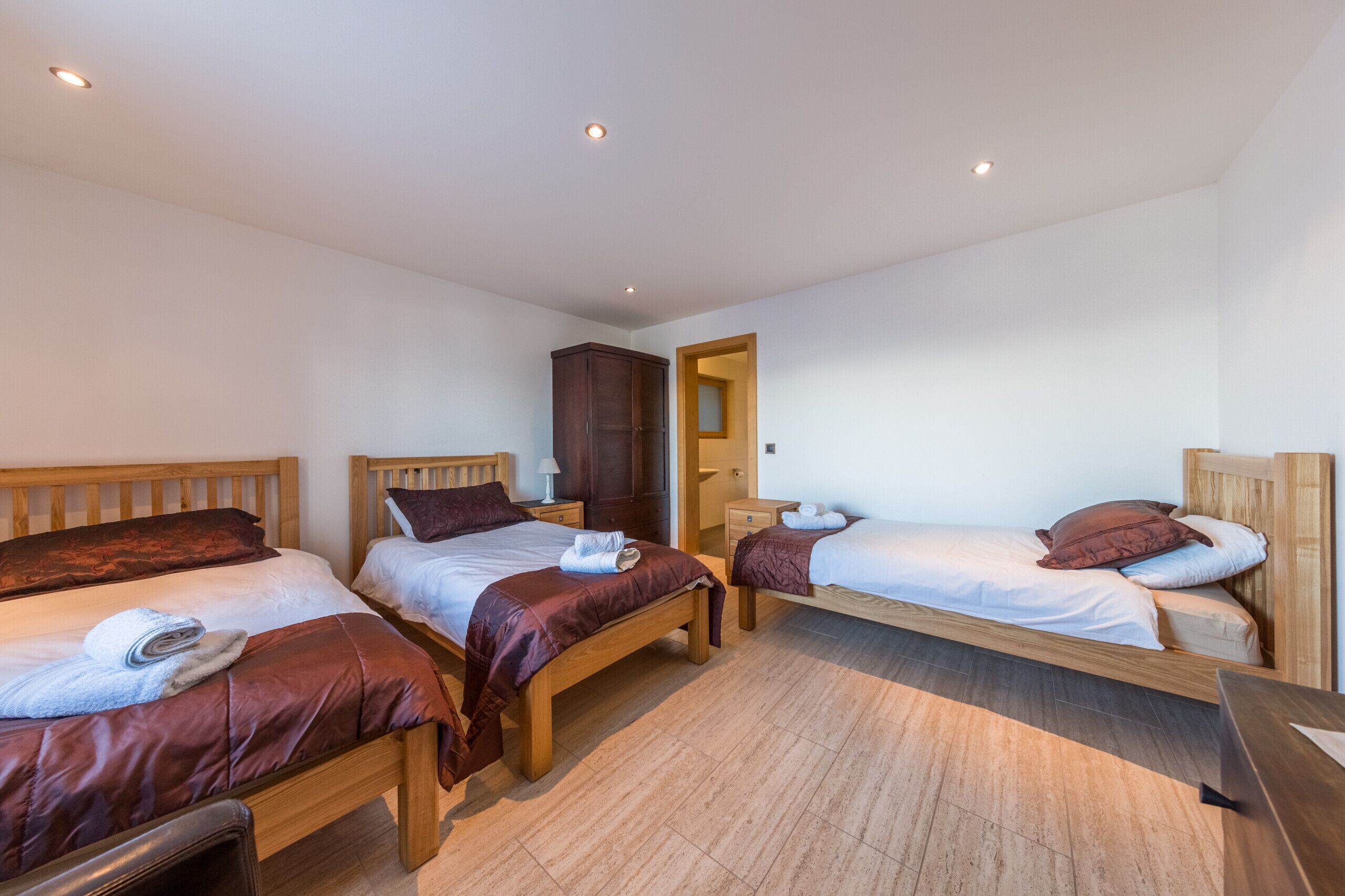 A room with three wooden beds, each with a headboard, a wooden wardrobe, and a wooden desk.