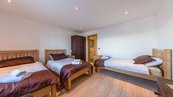A room with three wooden beds, each with a headboard, a wooden wardrobe, and a wooden desk.