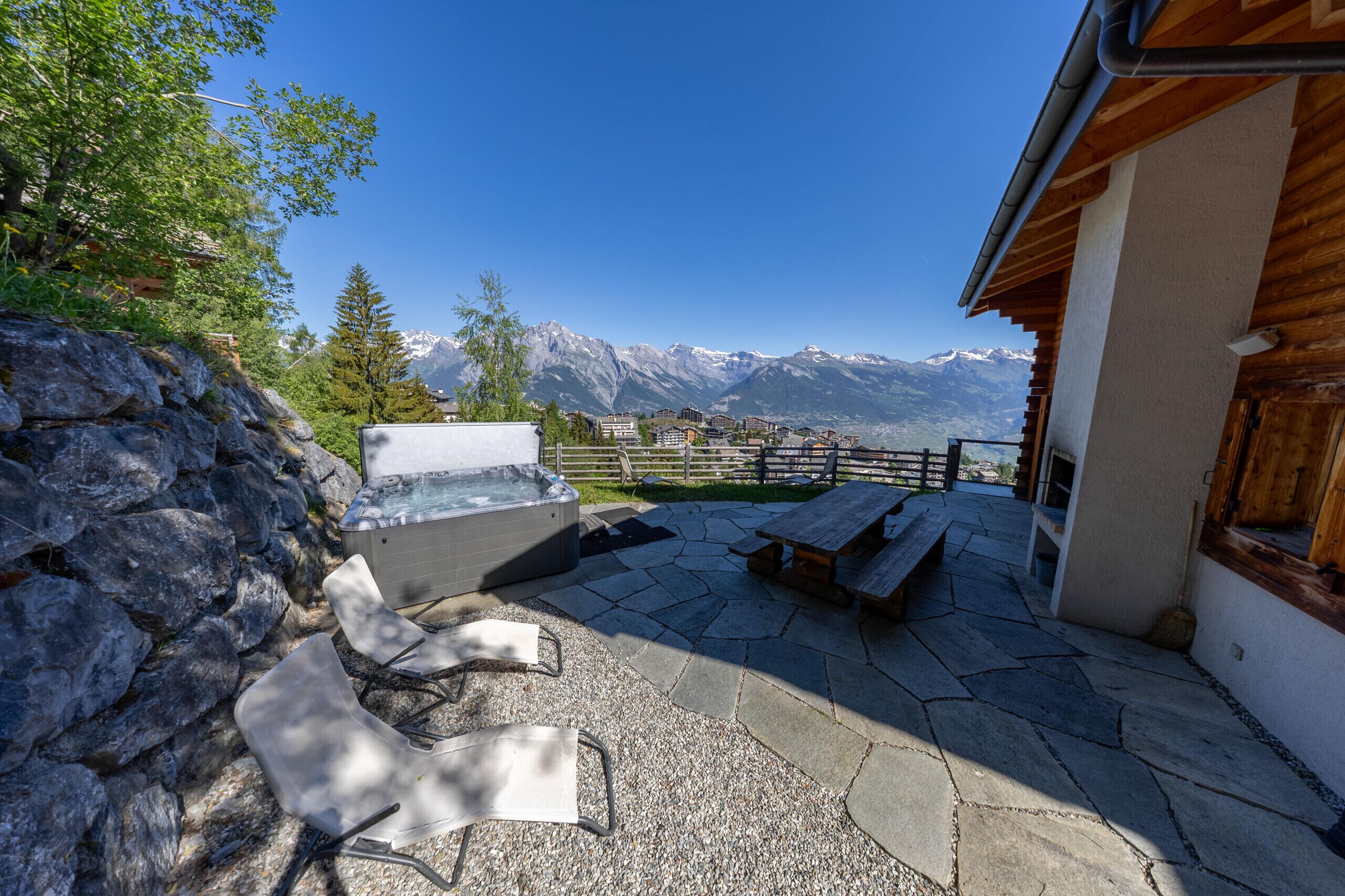 A patio with stone flooring, a hot tub, and wooden furniture.