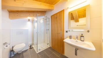 A modern bathroom with a glass shower, wooden ceiling, white tiles, and a wooden door.