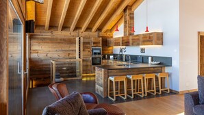 A modern kitchen with wooden beams, a central island with bar stools, and a red pendant light. - Grimpeur luxury duplex, Spa Access, in front of th (Haute-Nendaz)
