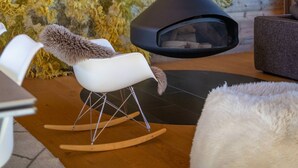 A modern interior with a stone wall, a large chimney, and a cozy seating area with a rocking chair and a fluffy rug. - Grimpeur luxury duplex, Spa Access, in front of th (Haute-Nendaz)