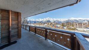 Ein Holzbalkon mit Blick auf schneebedeckte Berge und eine darunterliegende Stadt.