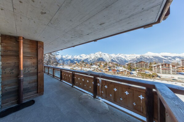 A wooden balcony with a view of snow-covered mountains and a town below.