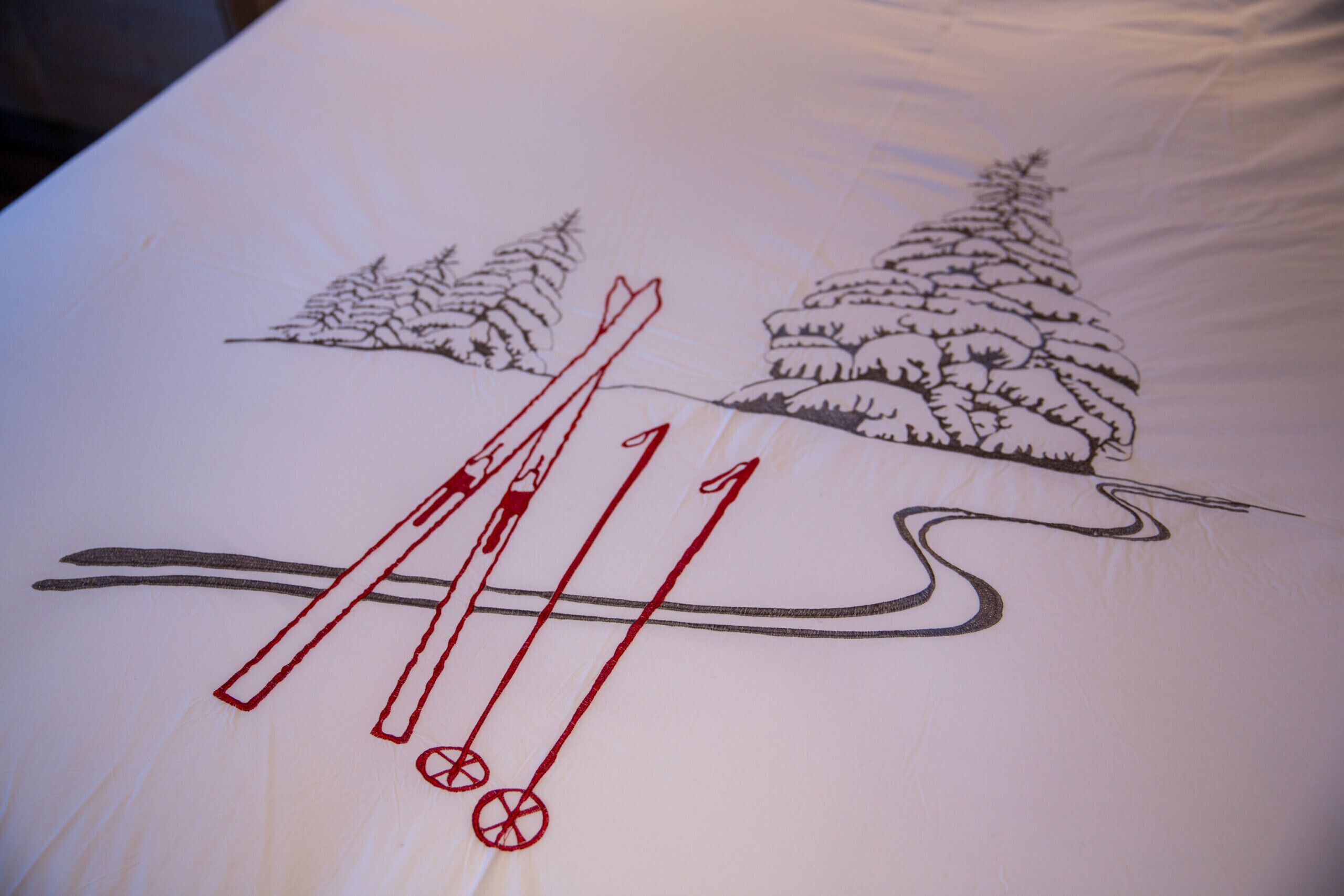 En seng med et illustrationstema med ski, skiudstyr og sneklædte træer.