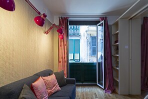A room with a sofa, a red desk lamp, a door leading to an outdoor area, and a shelving unit. - Design in Genoa city center by Wonderful Italy (Genova)