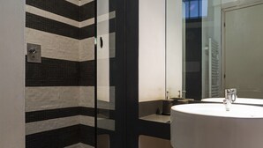 A modern bathroom with a black and white striped tile wall, a glass shower enclosure, and a round sink with a mirror. - Design in Genoa city center by Wonderful Italy (Genova)