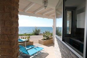 A covered patio with a view of the sea, a stone pillar, and a kitchen area with cabinets and a stove.