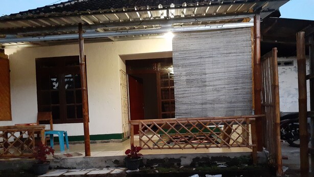 A traditional house with a tiled porch, a wooden fence, and a motorcycle parked outside.