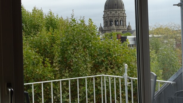 A view of a building with a dome and a cross on top, seen through foliage. - bright apartment in the lively, cultural city of Mainz (Rheinland-Pfalz)