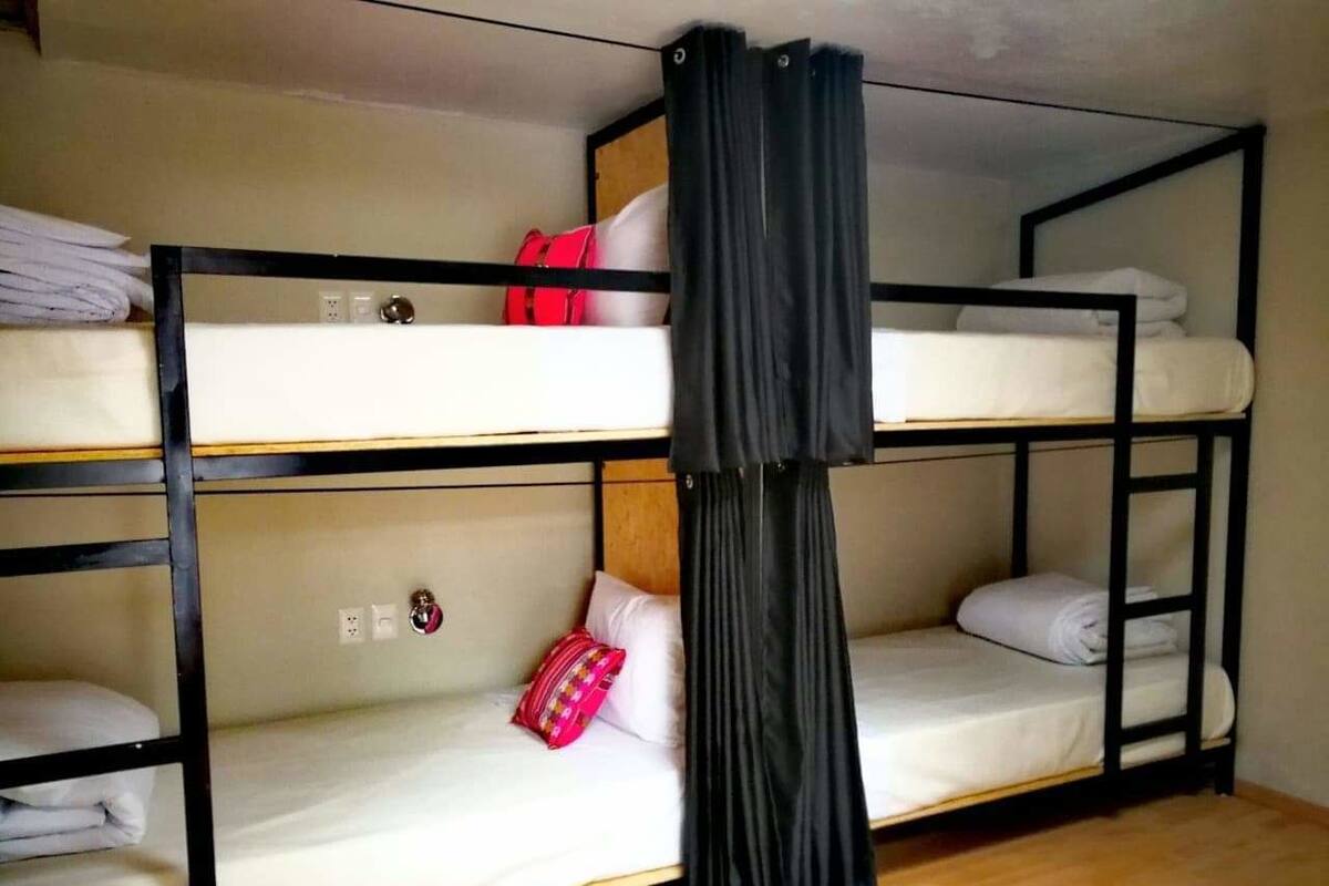 Habitación con literas, una cortina negra, ropa de cama blanca y una bolsa roja en la litera superior.