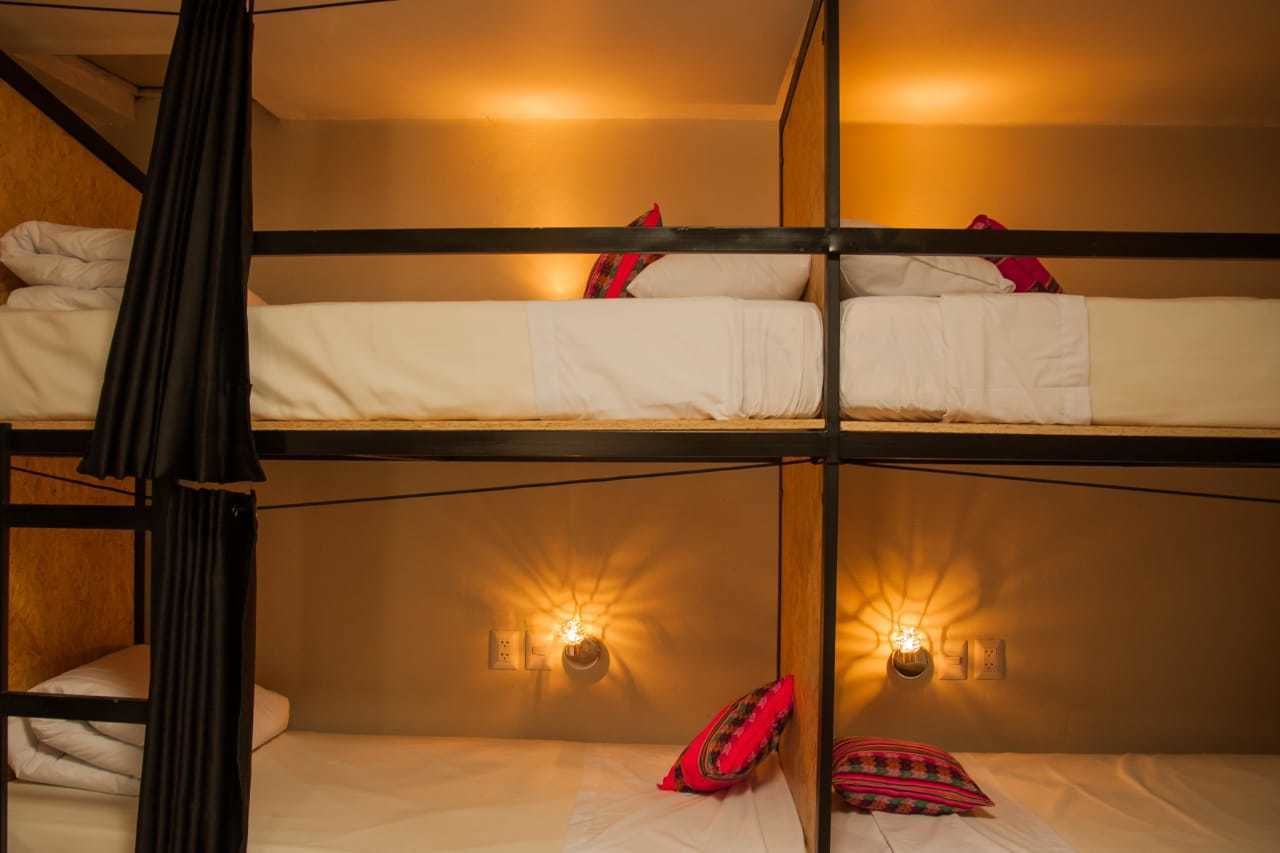 Une chambre avec un lit superposé, comportant deux lits, chacun avec une literie blanche et des oreillers rouges. Des lampes murales sont fixées de chaque côté des lits.