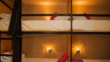 Une chambre avec un lit superposé, comportant deux lits, chacun avec une literie blanche et des oreillers rouges. Des lampes murales sont fixées de chaque côté des lits.
