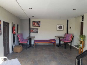 A spacious indoor area with two chairs and a bench, a fire extinguisher, and a framed picture on the wall. - Xplora Hostel Cusco (Cusco)