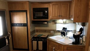 Cocina compacta para autocaravana con armarios de madera, un microondas, una estufa y un lavabo.