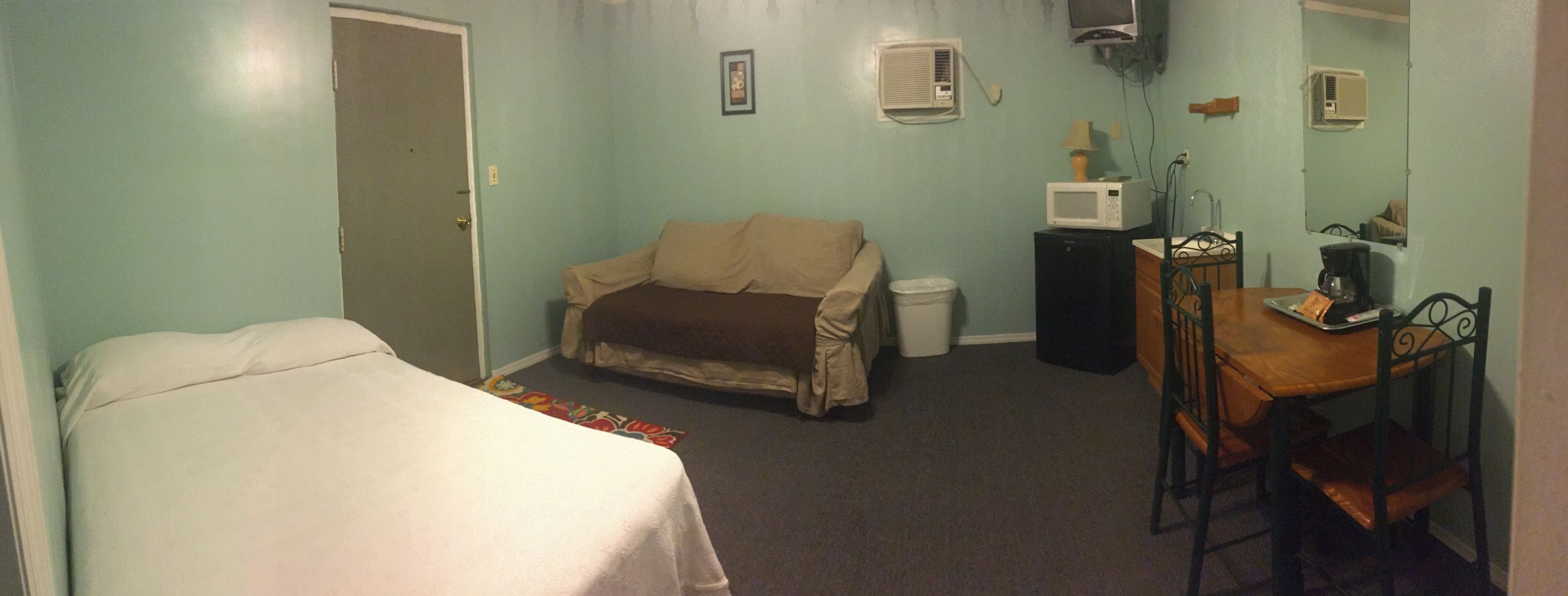 A room with a bed, a couch, a small table with a chair, a microwave, and a coffee maker.