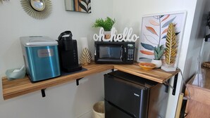 Una cocina compacta con un refrigerador azul, una cafetera negra, un microondas y un refrigerador pequeño negro.