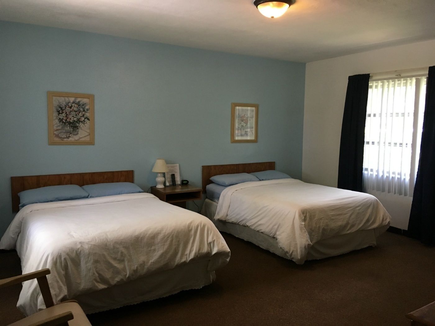 Une chambre avec deux lits simples, une table de chevet avec une lampe et une fenêtre avec des rideaux.