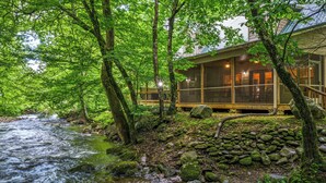 Une cabane avec vue sur une rivière, entourée d’arbres et de rochers.