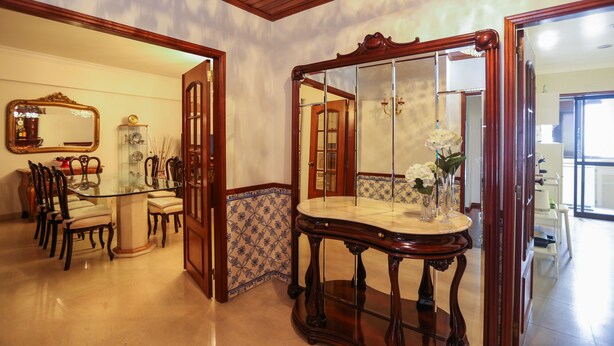 A dining area with a glass table, chairs, and a wooden side table with a mirror. - Wide and bright Apt (Lisboa)