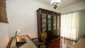 A room with a wooden desk, a green chair, a large dark wooden cabinet, and a chandelier. - Wide and bright Apt (Lisboa)
