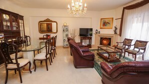 A traditional living room with a glass-top dining table, leather sofas, a chandelier, a television, and a fireplace. - Wide and bright Apt (Lisboa)