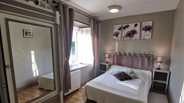 Une chambre avec un grand miroir, un lit recouvert d’une courtepointe blanche et agrémenté d’oreillers, deux lampes de chevet et une fenêtre avec des rideaux.