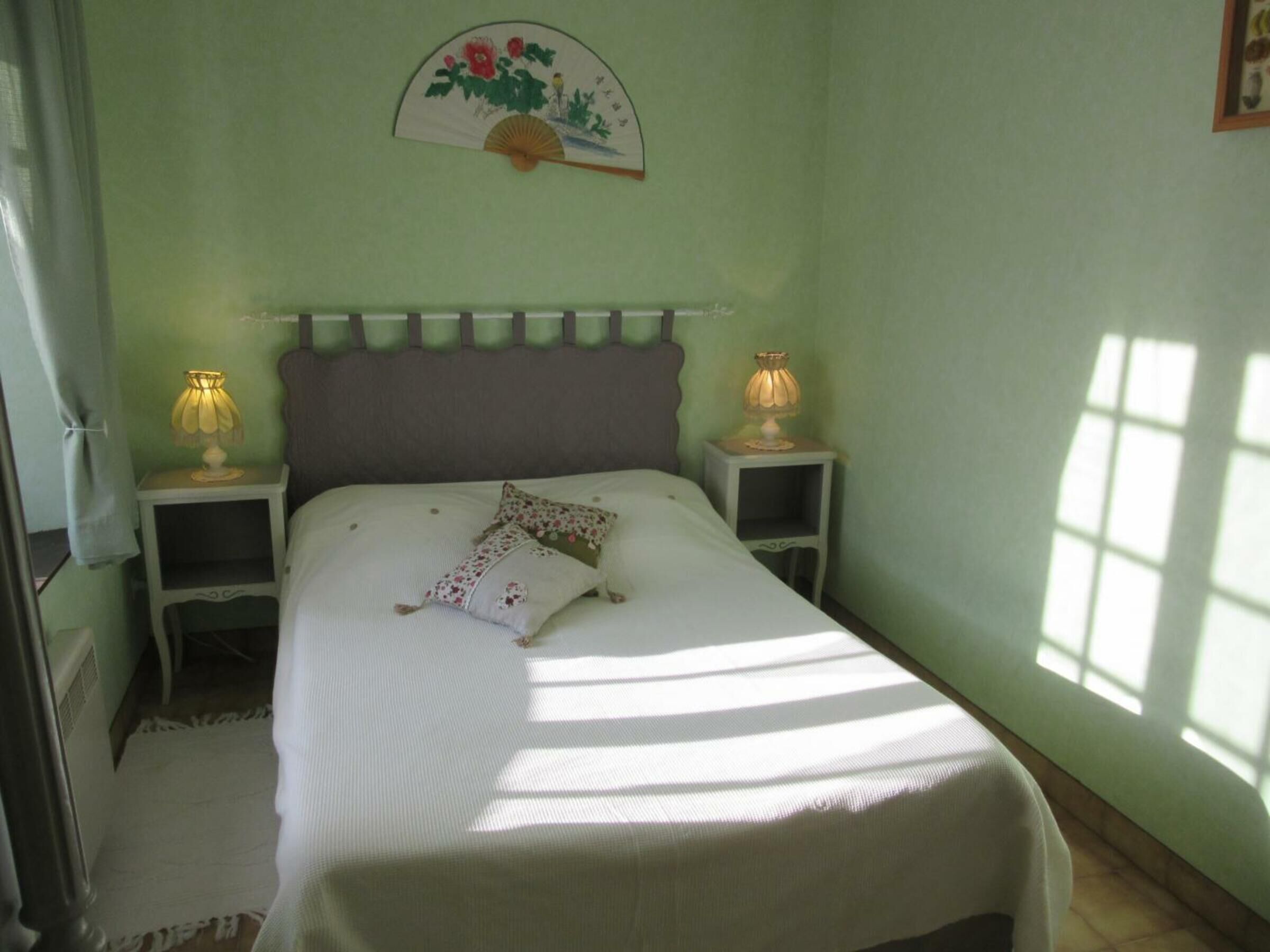 A bedroom with a bed, two bedside tables with lamps, a wall hanging, and a window.