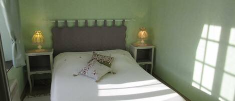A bedroom with a bed, two bedside tables with lamps, a wall hanging, and a window.
