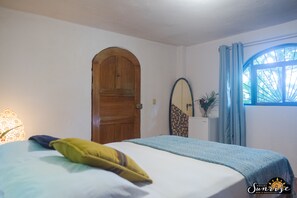 A bedroom with a bed, a wooden door, a mirror, and a window with curtains.