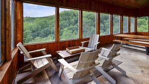 A wooden cabin with large windows overlooking a forest. There are three Adirondack chairs and a picnic table. - Fabulous Mountain Views, Secluded, Luxurious , Arcades, Theater, More (Gatlinburg)