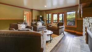 A cozy living room with a fireplace, comfortable seating, and large windows offering a view of the outdoors. - Fabulous Mountain Views, Secluded, Luxurious , Arcades, Theater, More (Gatlinburg)