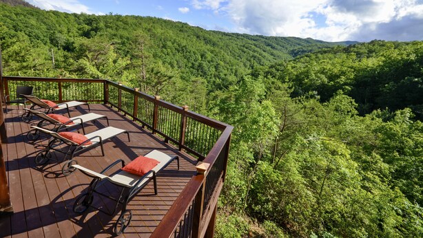 A deck with lounge chairs and a railing overlooking a forested valley. - Fabulous Mountain Views, Secluded, Luxurious , Arcades, Theater, More (Gatlinburg)