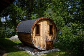 A wooden barrel-shaped building with two windows and a door, surrounded by greenery. - Chalet Pierre Blanche - Ski-in/out (Haute-Nendaz)