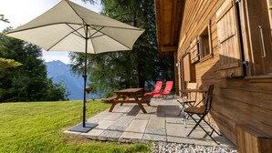 A wooden cabin with a picnic table and chairs, a large umbrella, and a view of mountains. - Chalet Pierre Blanche - Ski-in/out (Haute-Nendaz)
