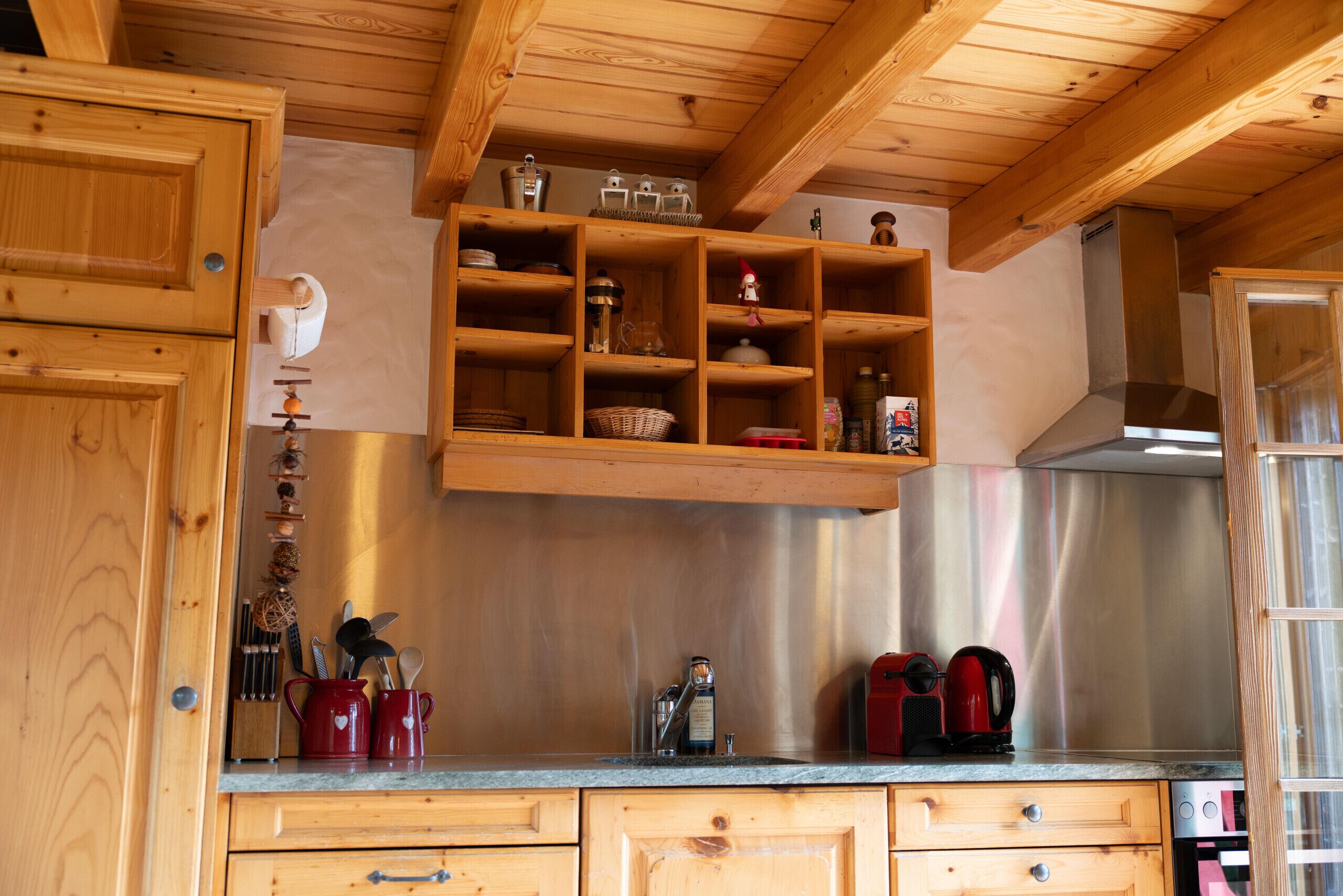 A kitchen with wooden cabinets, a stainless steel range hood, and a built-in shelf with various kitchen items.