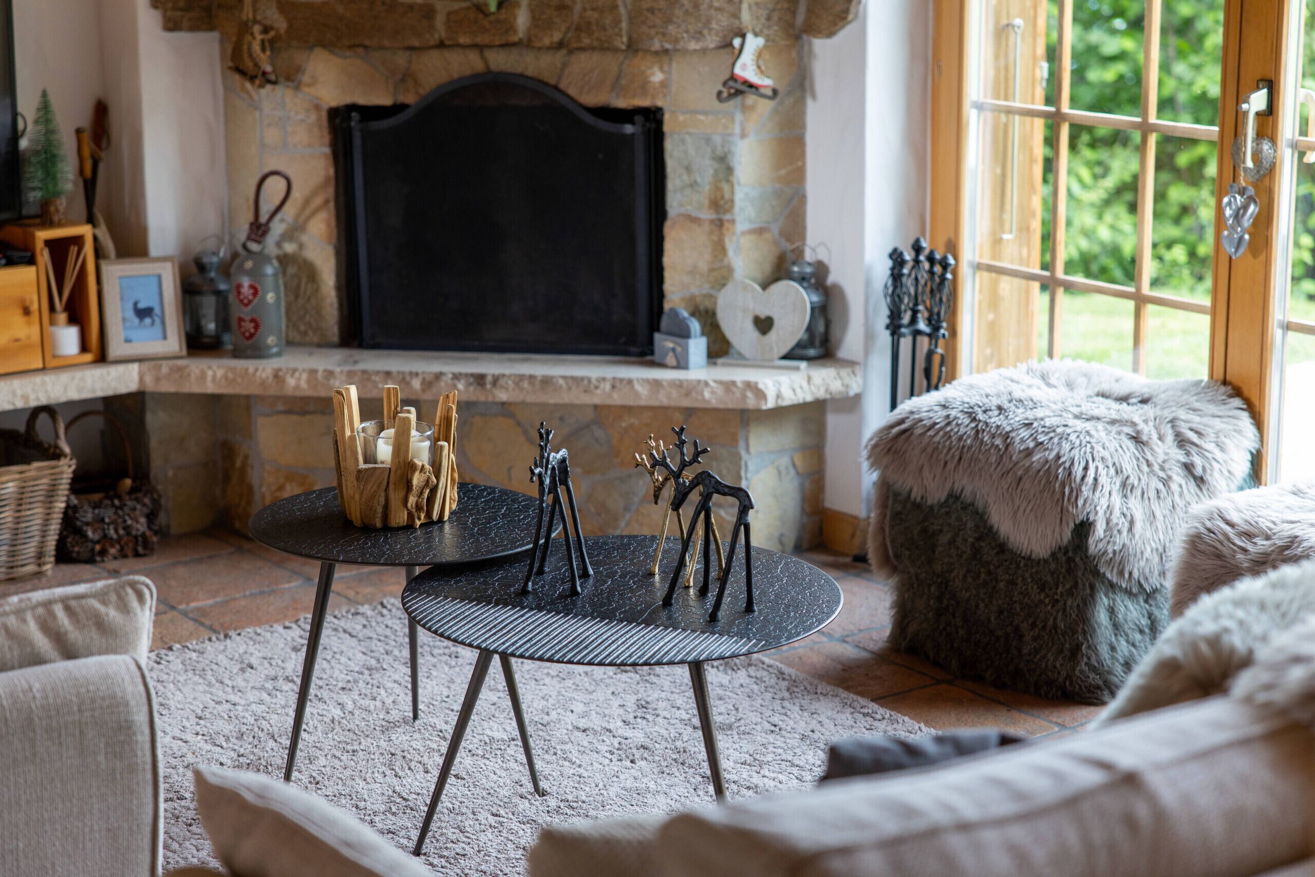 Una sala de estar acogedora con chimenea de piedra, una mesa redonda con velas y un otomano mullido.