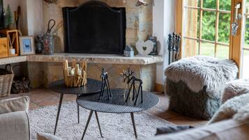 Una sala de estar acogedora con chimenea de piedra, una mesa redonda con velas y un otomano mullido.