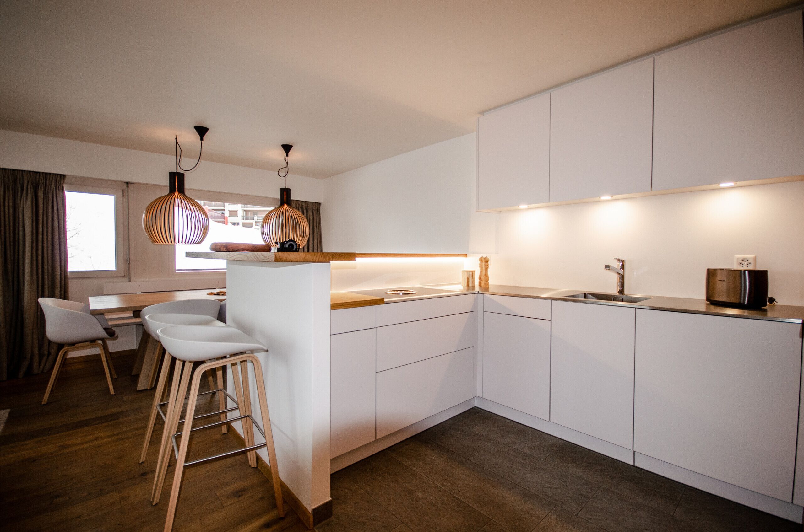 A modern kitchen with white cabinets, a wooden countertop, and two hanging pendant lights.