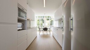 A modern kitchen with white cabinetry, a built-in microwave, and a dining area with a table and chairs. - Treasure | The Rentals Collection (San Sebastián)