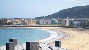 A coastal cityscape with a sandy beach, a large Ferris wheel, and historic buildings along the waterfront. - Treasure | The Rentals Collection (San Sebastián)