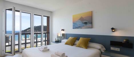 Une chambre à coucher avec un grand lit, deux oreillers, une table de chevet, une étagère fixée au mur et un tableau.