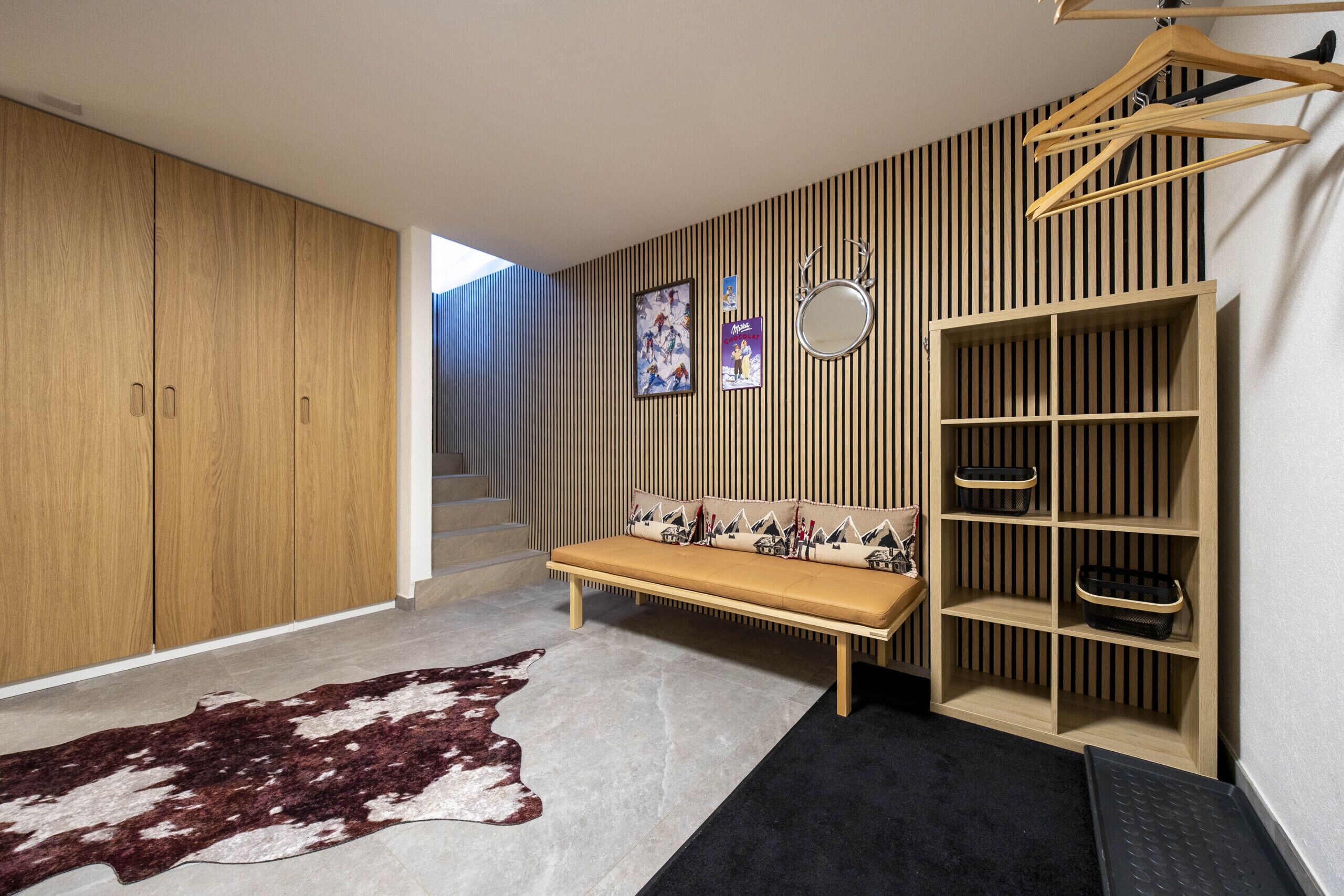 Ein modernes Zimmer mit einem Holzschrank, einer Bank mit gemusterten Kissen, einer Kleiderstange und einer gestreiften Wand.